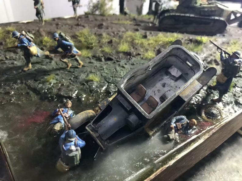 May include: A detailed diorama depicting a World War I scene with miniature soldiers in blue uniforms, a damaged tank, and a small vehicle. The scene is set in a muddy environment with water and vegetation.