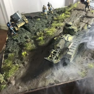 May include: A detailed diorama depicting a military scene with a camouflaged tank moving up a hill. Miniature soldiers are positioned around the tank and on the hillside. Smoke effects add to the realism of the scene. The tank is approximately 10 inches long.