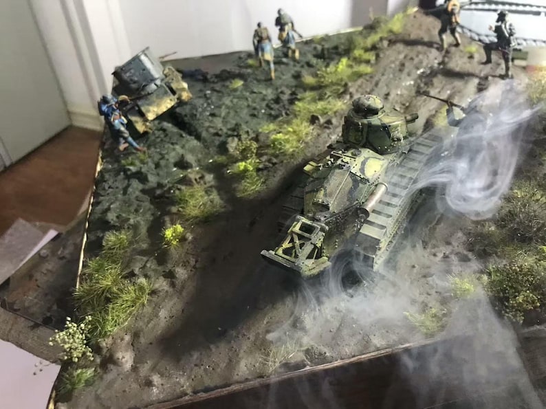May include: A detailed diorama depicting a military scene with a camouflaged tank moving up a hill. Miniature soldiers are positioned around the tank and on the hillside. Smoke effects add to the realism of the scene. The tank is approximately 10 inches long.