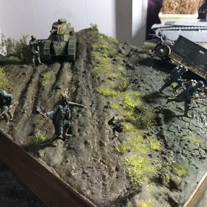 May include: A detailed diorama depicting a World War I battle scene. A tank ascends a muddy hill, while soldiers and a vehicle are positioned on the terrain. The scene is set with miniature figures and foliage, creating a realistic war environment.