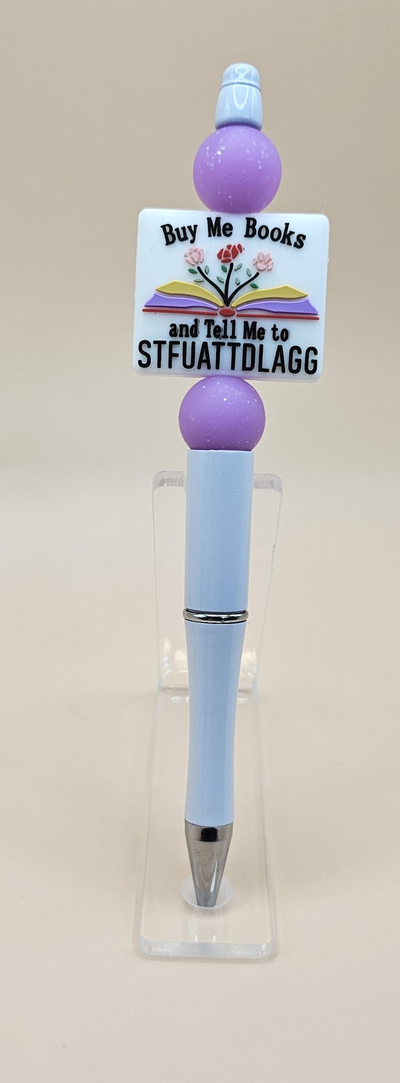 May include: A purple and white pen with a charm that says "Buy Me Books and Tell Me to STFUATTDLAGG".