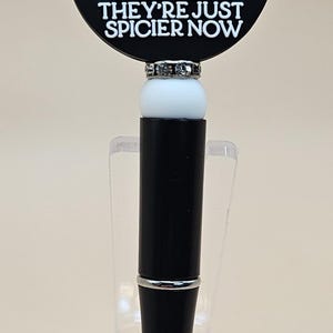 May include: Black and white pen with a round black and white charm that says "I still read fairytales they're just spicier now". The charm features a white castle and book with stars.