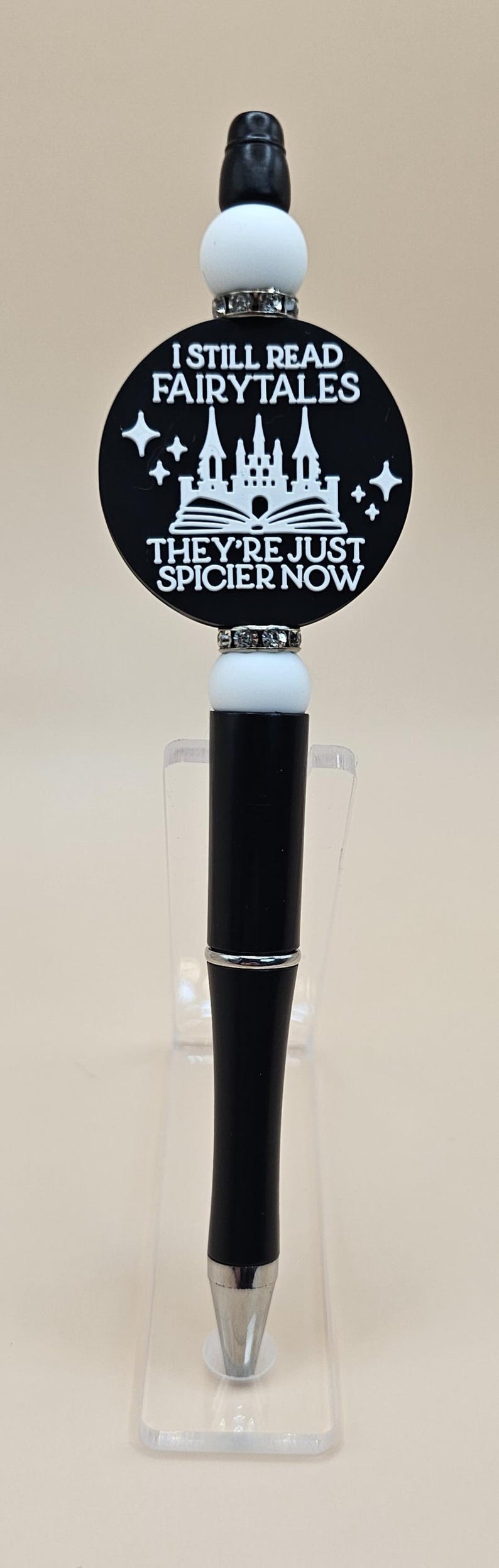May include: Black and white pen with a round black and white charm that says "I still read fairytales they're just spicier now". The charm features a white castle and book with stars.
