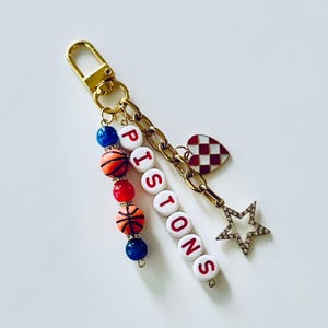 Llavero de baloncesto de los Pistons: llavero con cuentas doradas, rojas y azules con dijes de estrella y corazón.