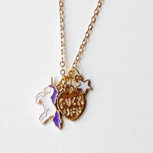 May include: Gold-colored necklace with a unicorn charm, a heart charm with the words "FUCK OFF", and a star charm. The unicorn is white with purple accents. The heart and star are white and gold.