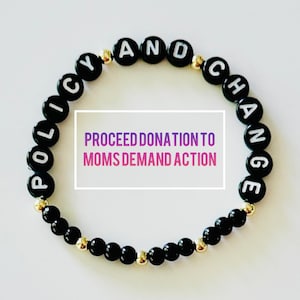 May include: A black beaded bracelet with white letter beads spelling "POLICY AND CHANGE." Gold-colored beads are interspersed. The image includes text that reads "PROCEED DONATION TO MOMS DEMAND ACTION."