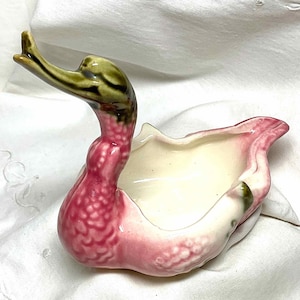 May include: A pink and green ceramic duck shaped dish. The duck has a raised head and a small bowl in the back. The duck is decorated with a floral pattern.