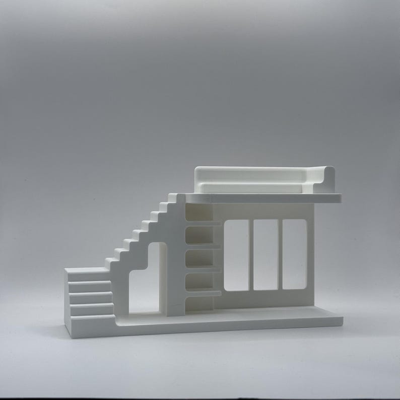 May include: A white architectural model with a staircase, a multi-windowed facade, and a flat roof. The model has a minimalist design with clean lines and a modern aesthetic. The structure is made of a solid, opaque material.
