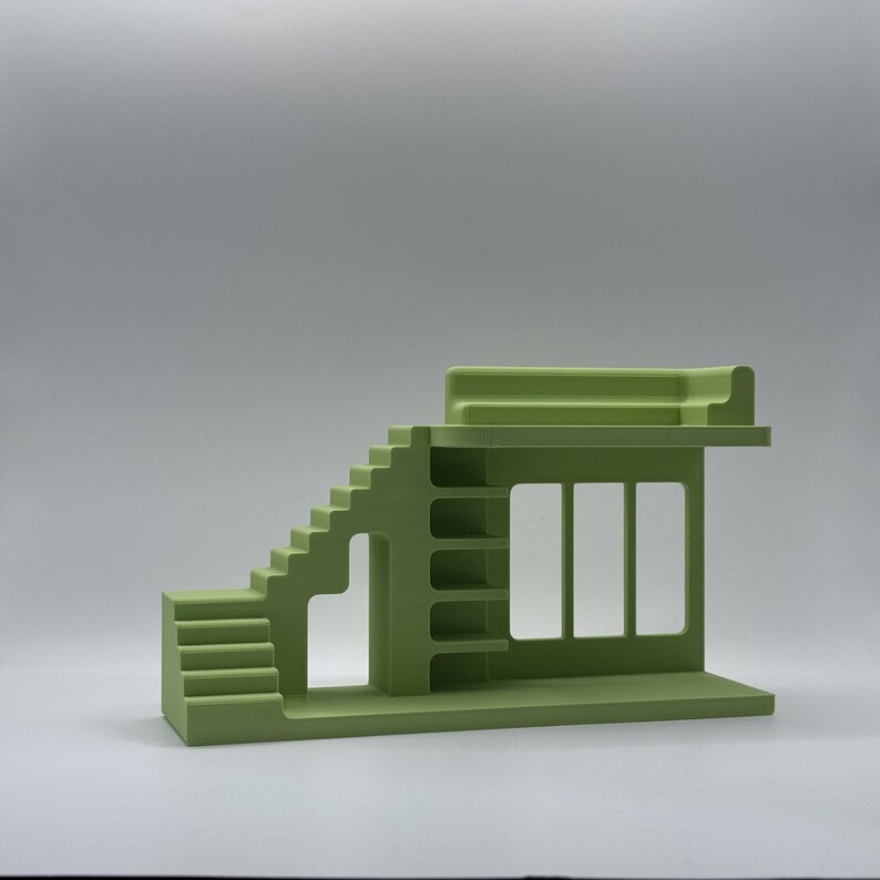 May include: A light green architectural model featuring stairs, a window, and shelves. The model has a flat roof and a rectangular base. The design is minimalist and geometric, with clean lines and a solid colour.