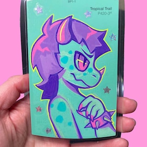 Op de afbeelding: Illustratie van een turquoise en paars cartoonpersonage op een kleurstalenkaart. Het personage heeft een spiked kraag en steraccenten. Tekst op de kleurstalenkaart luidt "Tropical Trail P420-3M" en "BP1-1".