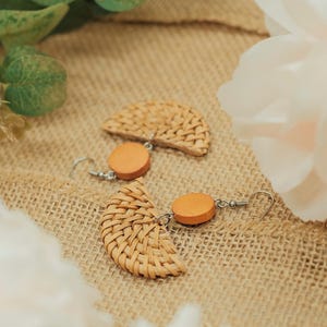 May include: A pair of woven wood earrings with a round wooden accent. The earrings are on a brown burlap background.
