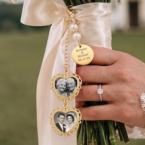 May include: A gold-toned wedding bouquet charm featuring two heart-shaped frames with black and white photos, a round disc engraved with "Brittany & Michael 06-11-26", and white pearl accents, all attached to a cream satin ribbon on a floral bouquet.