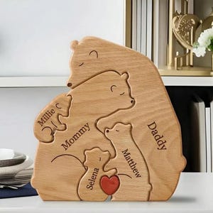 May include: Wooden family bear puzzle with the words "Mommy", "Daddy", "Millie C", "Matthew", and "Selena" engraved. A red heart is in the center. The puzzle is made of light-colored wood and is designed to interlock.