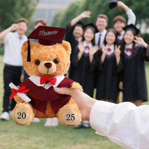 May include: A plush teddy bear wearing a graduation gown, cap with the name "Mason", and a red bow tie. The bear holds a diploma tied with a red ribbon. The numbers "20" and "25" are on the bear's feet. A group of graduates are in the background.