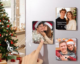 Könnte beinhalten: Quadratische Magnete mit Fotos von Paaren mit Weihnachtsmützen sind an einem Kühlschrank angebracht. Jeder Magnet hat eine Musikplayer-Oberfläche mit dem Text "Because You Live". Ein Weihnachtsbaum und Geschenke sind im Hintergrund zu sehen.