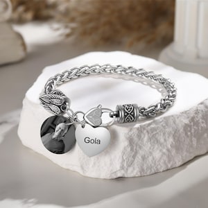 Może przedstawiać: Srebrna bransoletka z plecionym łańcuszkiem, zawieszką w kształcie serca z grawerem "Gola", okrągłą zawieszką ze zdjęciem i zawieszką z anielskimi skrzydłami.