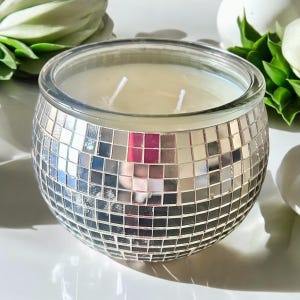 May include: A round, silver candle holder with a mirrored mosaic design. The candle holder is filled with a white candle.