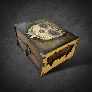 May include: A wooden box with a carved owl design on the lid. The box is stained in shades of brown and features a metal clasp. The front of the box has a unique cut-out design.