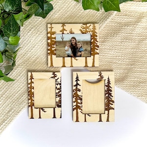 Puede incluir: Tres marcos de fotos de madera con acabado de madera natural. Los marcos presentan un diseño de árbol cortado con láser en los bordes. Un marco contiene una foto familiar. Los marcos son de varios tamaños, ideales para exhibir fotos familiares o obras de arte.