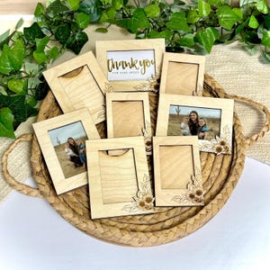 Puede incluir: Una colección de pequeños marcos de fotos de madera de color claro, algunos con fotos y otros en blanco. Un marco muestra el texto "thank you for your order" en letras doradas. Varios marcos están decorados con diseños de girasoles cortados con láser, dispuestos en una cesta tejida.
