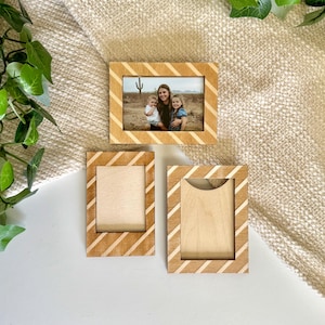 Puede incluir: Tres marcos de fotos de madera con un diseño de rayas diagonales. Un marco contiene una foto familiar, los otros dos están vacíos. Los marcos son de madera clara con un acabado natural.