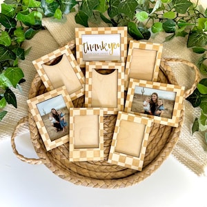 Puede incluir: Una colección de marcos de fotos de madera con un patrón de cuadros, algunos con fotos y uno con el texto dorado "thank you for your order". Los marcos están dispuestos en una cesta tejida.