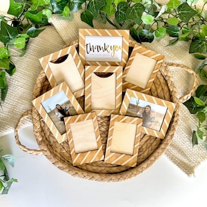 Puede incluir: Una colección de pequeños marcos de fotos de madera con un diseño de rayas diagonales en una cesta tejida. Algunos marcos contienen fotos, mientras que uno muestra el texto "thank you for your order" en dorado.
