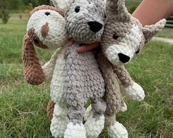 Peut inclure: Trois peluches faites à la main en crochet représentant des chiens de différentes couleurs. Un chien est marron et blanc, le second est gris et blanc, et le troisième est beige et blanc. Les chiens ont des yeux et des nez noirs, présentés sur de l'herbe verte.