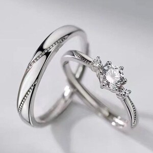 May include: Two silver rings. One ring has a row of small stones set into the band. The other ring has a large, clear, round stone in the centre, with smaller stones either side.