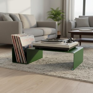 May include: A dark green metal record player stand with an integrated vinyl storage slot. The stand holds a white and black turntable on the top surface and a collection of vinyl records in the side compartment, featuring the text Gaoxar Dan.