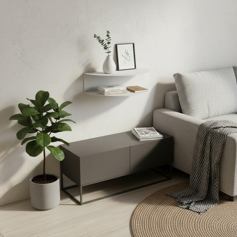 May include: A modern living room scene featuring a gray cabinet with a black metal frame, a white wall-mounted shelf, and a gray sofa. A potted plant with large green leaves and a round woven rug add natural elements to the space.