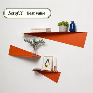 Può includere: Set di tre mensole da parete in metallo arancione dal design geometrico. Le mensole sono montate su una parete bianca e contengono oggetti decorativi come libri, piante, un vaso e un quadro incorniciato. Il testo "Set of 3 - Best Value" è in un ovale verde e bianco.