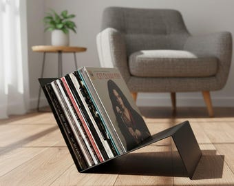 May include: A matte black metal vinyl record storage rack holding a collection of various music albums. The rack features an angled design that supports the records in an upright position, displaying the front cover of the first record.