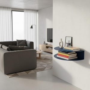May include: A modern living room with a dark gray sectional sofa, a wooden coffee table, and a wall-mounted navy blue shelf. The shelf holds books, a framed picture, and a decorative vase. The room has a neutral color palette with white curtains and a geometric rug.