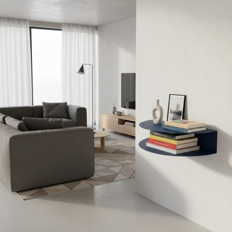 May include: A modern living room with a dark gray sectional sofa, a wooden coffee table, and a wall-mounted navy blue shelf. The shelf holds books, a framed picture, and a decorative vase. The room has a neutral color palette with white curtains and a geometric rug.