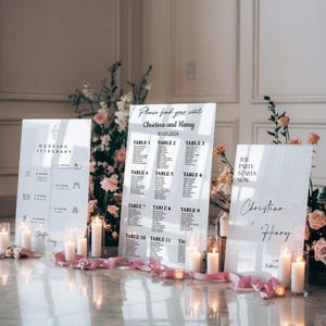 May include: White acrylic wedding signage with black text. The signs include a wedding itinerary, seating chart, and a sign that says "The party starts now." The signs are decorated with flowers and candles.