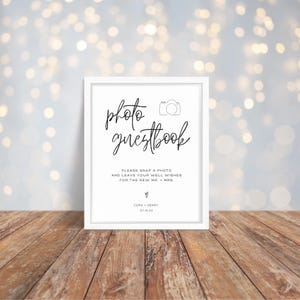 Może przedstawiać: Biały znak z czarnym tekstem, który brzmi "photo guestbook". Ikona aparatu znajduje się nad tekstem. Znak zawiera również tekst "Please snap a photo and leave your well wishes for the new Mr. & Mrs. Cora + Henry 07.15.XX"