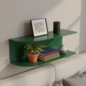 May include: A modern, green wall shelf with two tiers, holding a framed abstract art print, a small potted plant, books, a black speaker, and a decorative vase. The shelf is mounted on a neutral-colored wall.