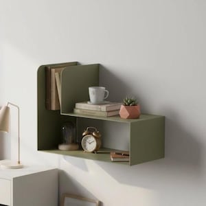 May include: An olive green wall-mounted shelf unit. It displays books, a white mug, a small succulent in a geometric pot, a vintage alarm clock, and a notebook. The shelf is mounted on a white wall.