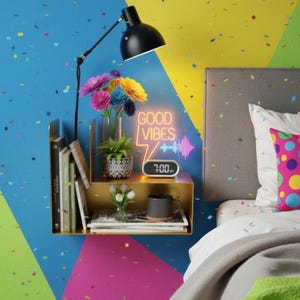 May include: A black desk lamp illuminates a gold shelf with books, flowers, and a digital clock displaying 7:00. The shelf also holds a mug and a neon sign that reads "GOOD VIBES". The wall is painted with blue, yellow, and pink geometric shapes.