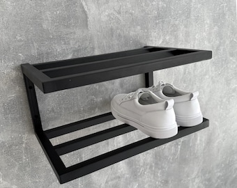 Può includere: Un portascape in metallo nero montato su una parete grigia. Il ripiano ha due livelli e contiene un paio di scarpe da ginnastica bianche. Il design è minimalista e moderno, adatto per l'ingresso o l'armadio.