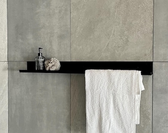 Può includere: Mensola in metallo nero montata su una parete piastrellata grigia. La mensola contiene un dosatore di sapone in vetro trasparente, una spugna beige e un asciugamano bianco. L'asciugamano è appeso.