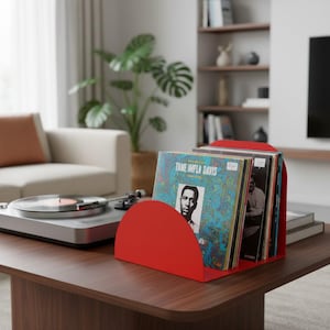 Könnte beinhalten: Ein leuchtend roter Schallplattenständer aus Metall mit halbkreisförmigem Seitenprofil, der mehrere Schallplatten enthält. Die vorderste Platte hat ein blau-grün marmoriertes Cover mit dem Text TAME IMPLA DAVIS und einem Porträt.