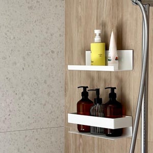 May include: Two white, wall-mounted shelves hold bathroom products. The top shelf has a yellow bottle and a tube of lotion. The bottom shelf displays three brown bottles and a clear, ribbed bottle. The shelves are against a wood-grain wall.