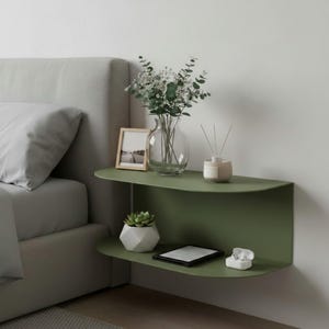 May include: An olive green, wall-mounted bedside table with two shelves. The top shelf features a clear glass vase with flowers, a framed photo, and a diffuser. The lower shelf displays a succulent in a white geometric pot, an e-reader, and white wireless earbuds.