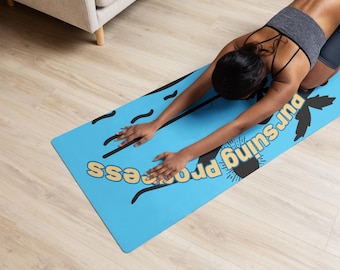 Puede incluir: Una esterilla de yoga azul con el texto "pursuing process" en amarillo y negro. Una persona está haciendo una pose de yoga en la esterilla.
