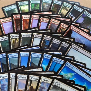 May include: A collection of Magic: The Gathering trading cards, featuring various land cards. The cards display images of forests, mountains, swamps, islands, and plains. The cards have black borders and text labels.