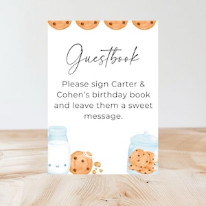 May include: White card with the text "Guestbook" in cursive. Below the text is a message that reads "Please sign Carter & Cohen's birthday book and leave them a sweet message." The card is decorated with cookies and milk.