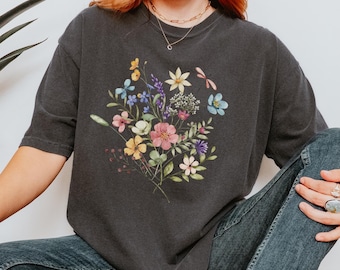 Può includere: Una maglietta grigia scura con una stampa floreale colorata. I fiori sono in tonalità di rosa, giallo, blu e verde. La maglietta è oversize e ha una vestibilità rilassata.