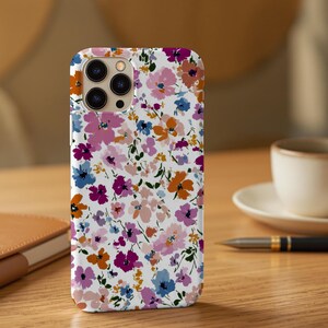May include: A white phone case with a colorful floral pattern. The design features a variety of flowers in shades of pink, purple, orange, and blue. The case has a glossy finish and a camera cutout.
